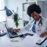 Woman doctor with stethoscope looking at medical papers at her office working hard